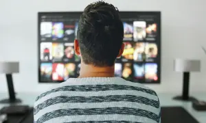 Mężczyzna w pasiastym swetrze ogląda na telewizorze menu aplikacji, gdzie widnieje logo Orange TV.