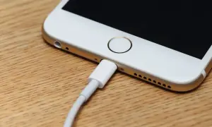 Zablokowany iPhone podłączony do komputera. Ekran jest czarny, a kabel ładujący wpięty do portu.