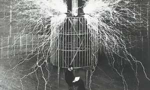 Nikola Tesla, siedzący w klatce, otoczony wyładowaniami elektrycznymi, pokazuje, kto wynalazł prąd.