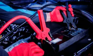 Mechanik w czerwonych rękawiczkach podłącza kable rozruchowe do akumulatora. Czy nowy akumulator trzeba ładować? Sprawdźmy!