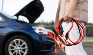 Osoba trzyma kable rozruchowe przy samochodzie z otwartą maską. Dowiedz się, jak podłączyć kable rozruchowe, by uruchomić auto.