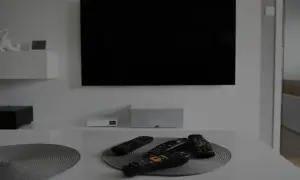 Na stole leżą piloty, a czarny ekran telewizora sugeruje, że jest brak obrazu.