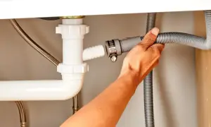 Ręka podłącza wąż odpływowy zmywarki do syfonu pod zlewem.