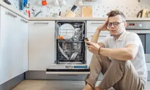 Zmartwiony mężczyzna szuka w telefonie informacji, jak zresetować zmywarkę Bosch, która stoi otwarta w kuchni.
