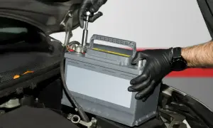 Mechanik w czarnych rękawiczkach montuje akumulator samochodowy. To kluczowy etap regeneracji akumulatora, zapewniający jego długą żywotność.