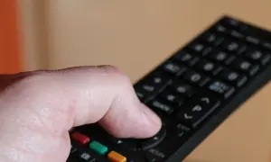 Dłoń naciska przycisk na pilocie, by dowiedzieć się, jak odbierać wszystkie kanały telewizji naziemnej.