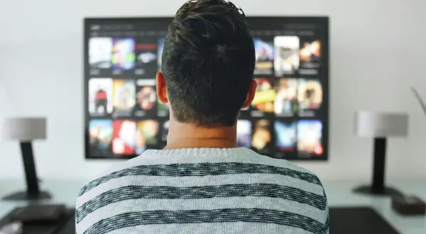 Mężczyzna w pasiastym swetrze ogląda na telewizorze menu aplikacji, gdzie widnieje logo Orange TV.