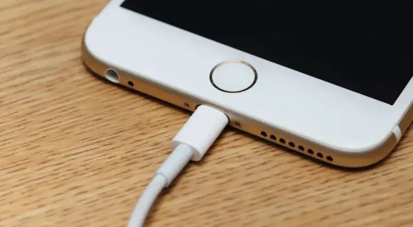 Zablokowany iPhone podłączony do komputera. Ekran jest czarny, a kabel ładujący wpięty do portu.