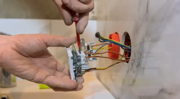 Ręce majsterkowicza przykręcają gniazdko. Widać przewody i puszkę instalacyjną. Poradnik: jak podłączyć gniazdko w starej instalacji.