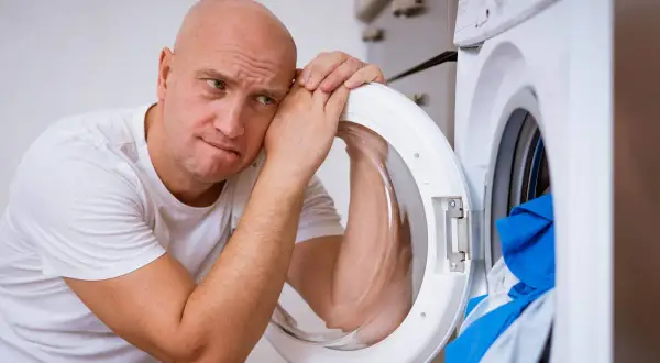Zmartwiony mężczyzna opiera głowę o otwarte drzwi pralki Whirlpool, która wyświetla błąd F05.