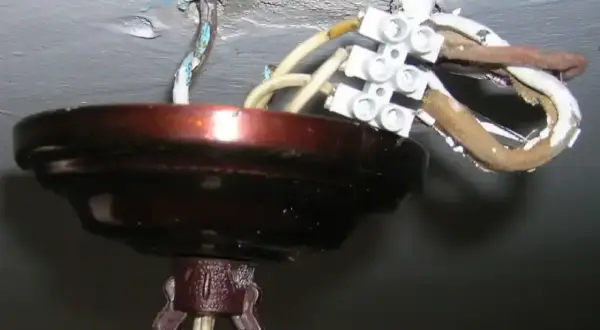 Podłączenie żyrandola: 3 kable z sufitu połączone w kostce. Widoczna metalowa osłona i fragment mocowania.