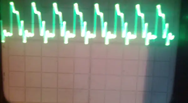 Zielone, kwadratowe fale na ekranie oscyloskopu, przypominające schodki.