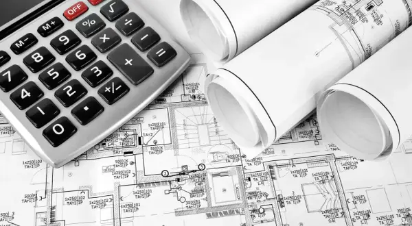 Kalkulator i zwinięte plany budowlane, wskazujące na planowanie koszt instalacji elektrycznej.