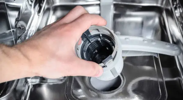 Ręka wyjmuje filtr zmywarki, który może być przyczyną, że zmywarka nie domywa naczyń.