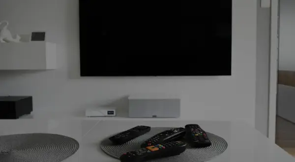 Na stole leżą piloty, a czarny ekran telewizora sugeruje, że jest brak obrazu.