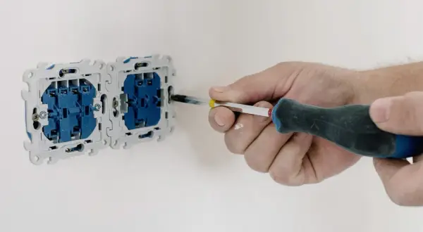 Elektryk wykonuje pomiar rezystancji izolacji gniazdek elektrycznych, dokręcając śrubokrętem elementy montażowe.