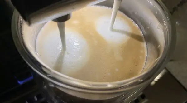 Mleko wylewa się z dyszy ekspresu DeLonghi, tworząc piankę na kawie. Niestety, ekspres DeLonghi nie spienia mleka tak, jak powinien.
