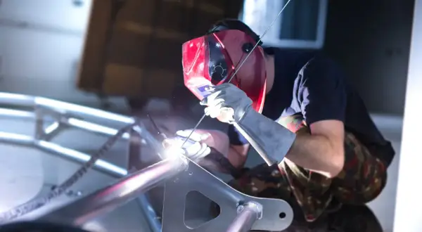 Spawacz w masce spawa aluminiową ramę. Widać jasny łuk spawalniczy i iskry. To pokazuje, czym spawać aluminium.