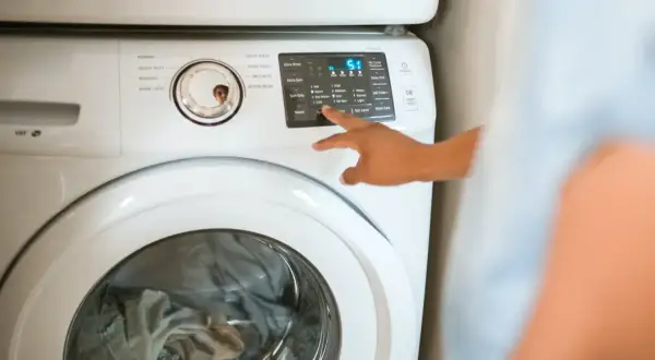 Ręka naciska przyciski na pralce Samsung, pokazując, jak zresetować pralkę Samsung.