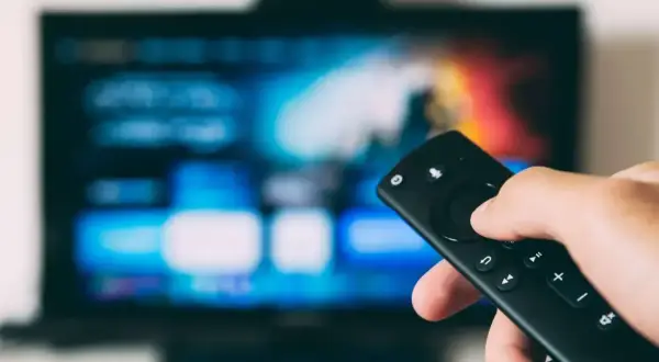 Dłoń trzyma pilot, celując w ekran telewizora. To przyszłość: telewizja naziemna bez anteny, dostępna cyfrowo.