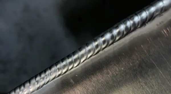 Precyzyjne spawanie aluminium migomatem. Widoczny gładki, lśniący ścieg spawalniczy na metalowej powierzchni.