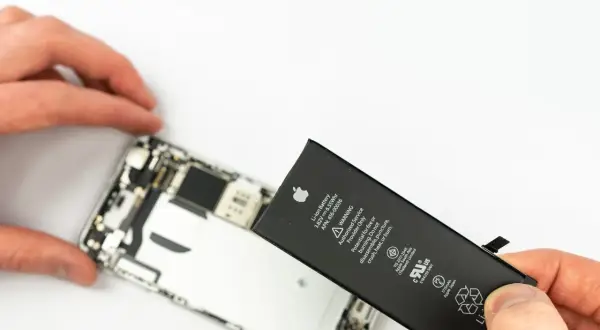 Wymiana iPhone'a jest potrzebna, gdy bateria jest zużyta. Dłonie trzymają nową baterię do iPhone'a obok otwartego telefonu.