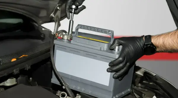 Mechanik w czarnych rękawiczkach montuje akumulator samochodowy. To kluczowy etap regeneracji akumulatora, zapewniający jego długą żywotność.
