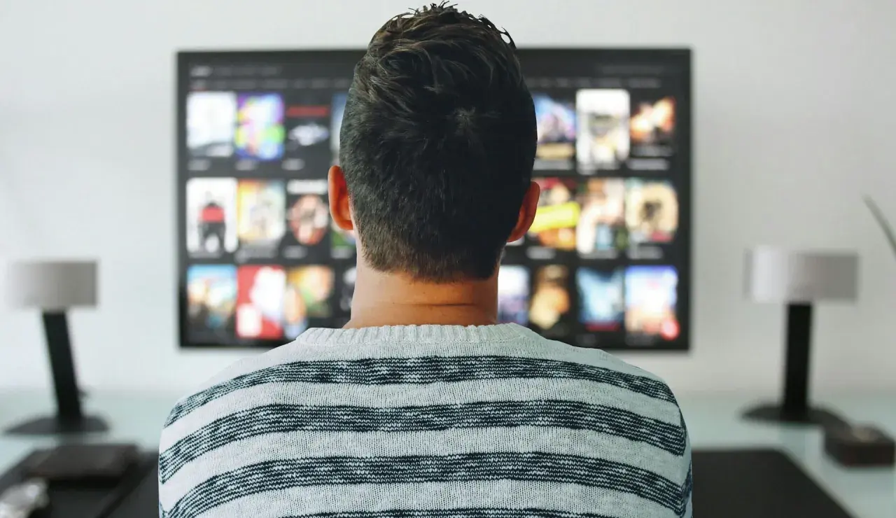 Mężczyzna w pasiastym swetrze ogląda na telewizorze menu aplikacji, gdzie widnieje logo Orange TV.