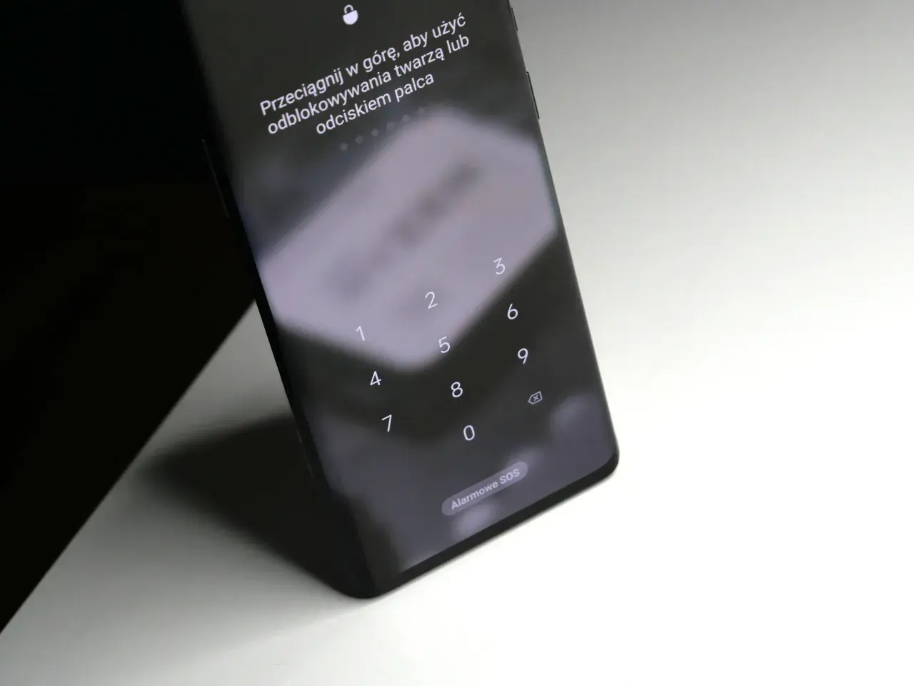 Ekran blokady telefonu z klawiaturą numeryczną i instrukcją "Przeciągnij w górę, aby użyć odblokowywania twarzą lub odciskiem palca". Jak odblokować telefon bez utraty danych?