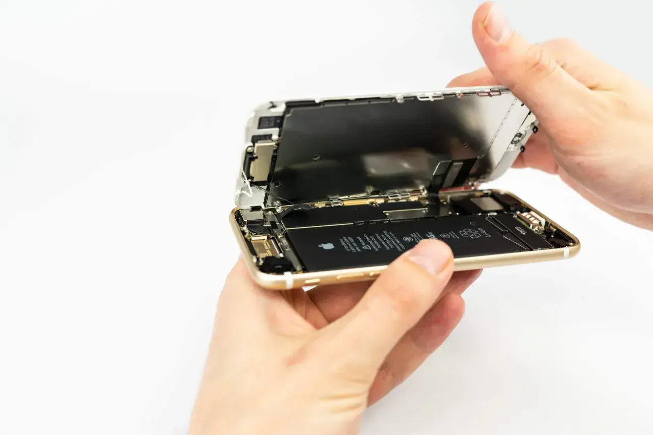 Dłonie rozkładają iPhone'a, odsłaniając baterię. Wymiana baterii iPhone 13 to proces, który można wykonać samodzielnie.