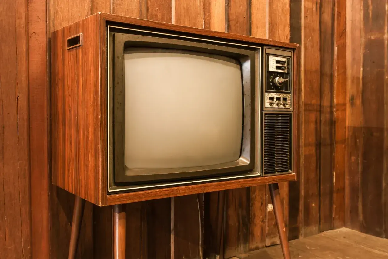 Stary telewizor z drewnianą obudową i ekranem kineskopowym. Prawdopodobnie pierwszy telewizor w domu, który gromadził całą rodzinę.