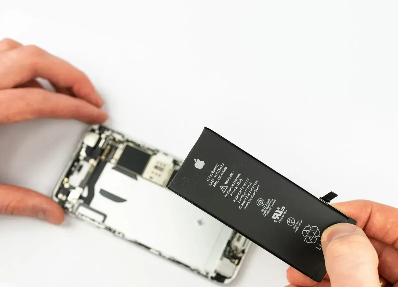 Wymiana iPhone'a jest potrzebna, gdy bateria jest zużyta. Dłonie trzymają nową baterię do iPhone'a obok otwartego telefonu.