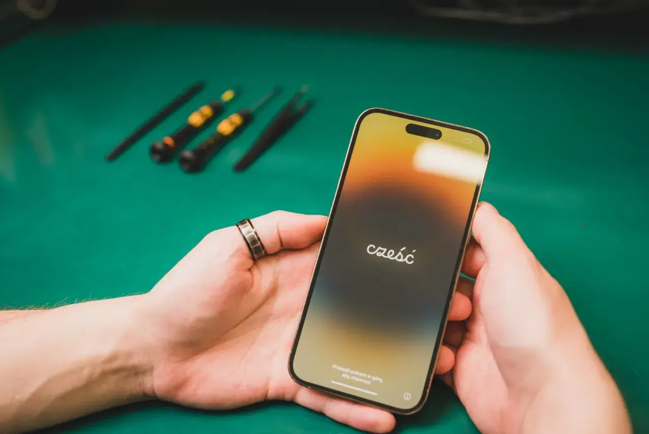 Dłonie trzymające iPhone'a z napisem "cześć" na ekranie, w tle narzędzia.