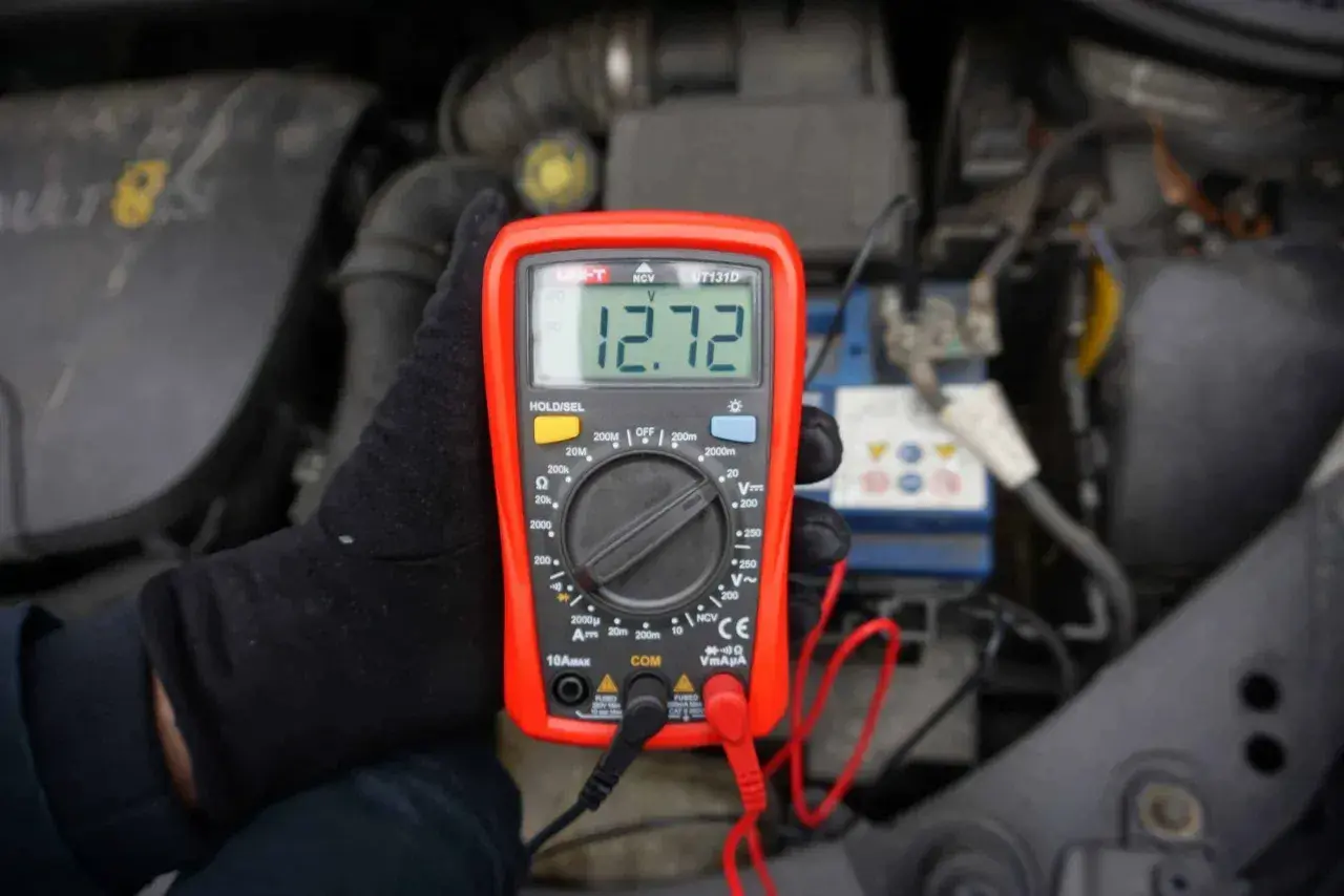 Sprawdzanie napięcia akumulatora 12V miernikiem. Wynik 12.72V.