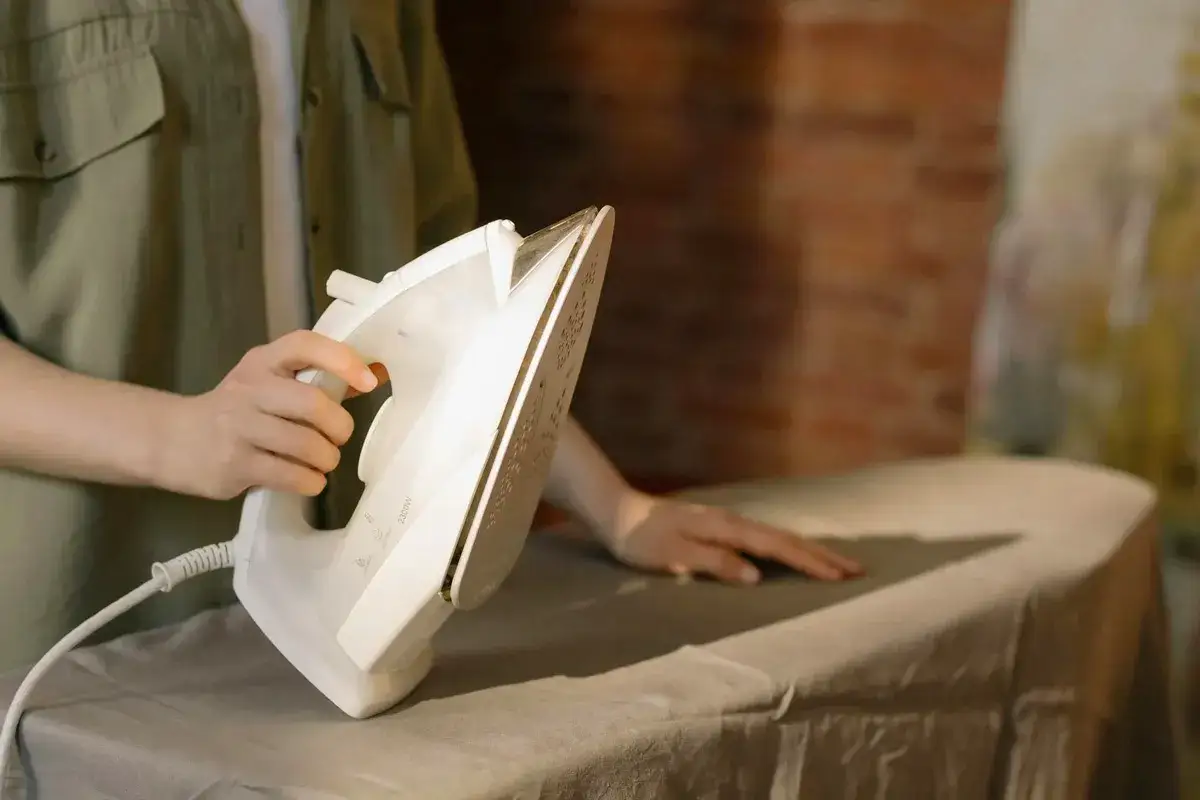 Odkamienianie żelazka Tefal jest proste. Dłoń trzyma białe żelazko nad deską do prasowania.
