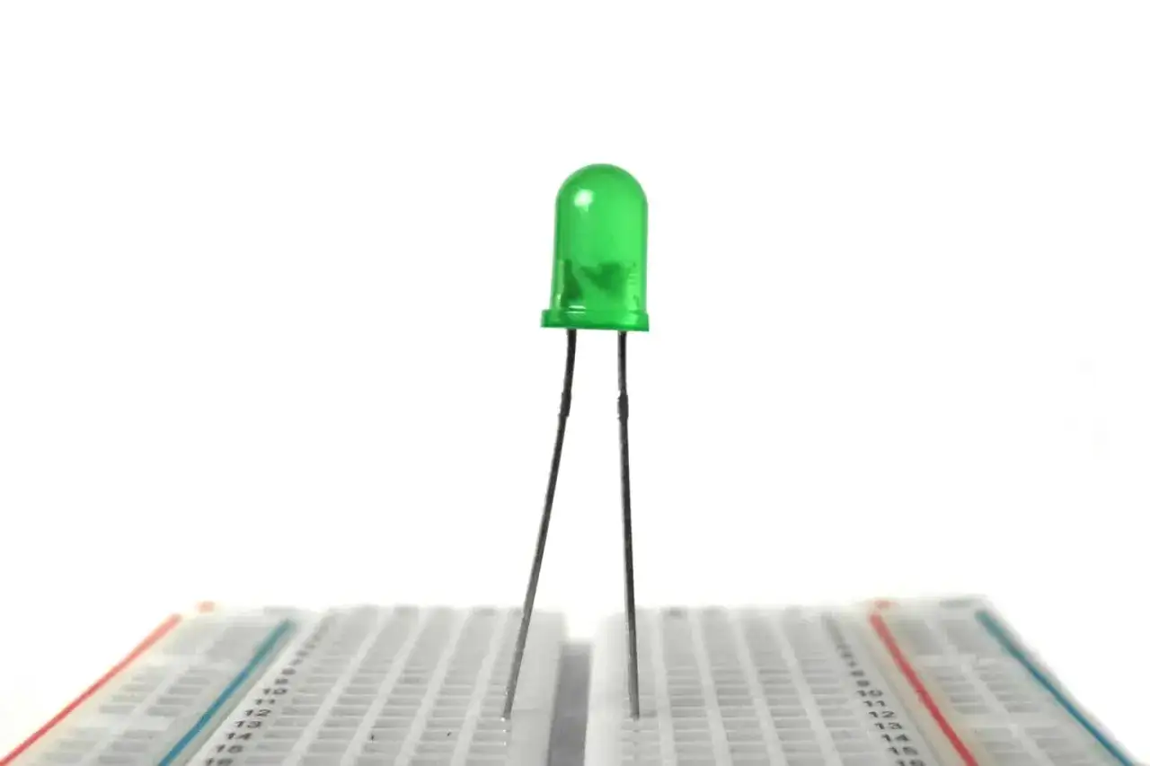 Zielona dioda LED stoi na płytce stykowej, gotowa do eksperymentów elektronicznych.