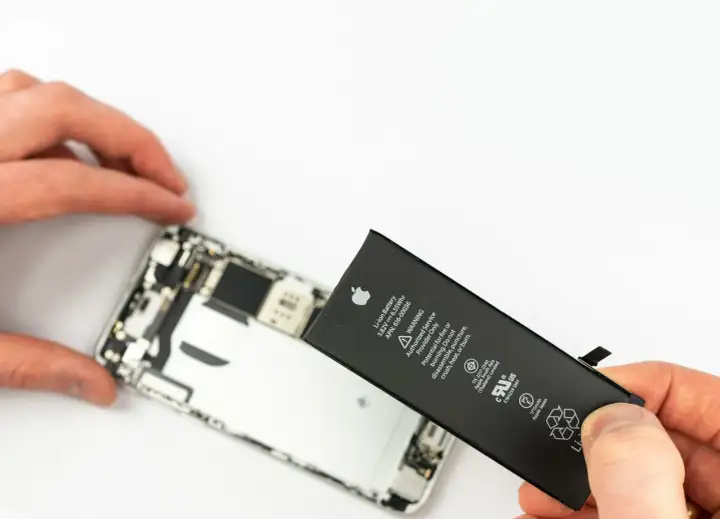 Wymiana iPhone'a jest potrzebna, gdy bateria jest zużyta. Dłonie trzymają nową baterię do iPhone'a obok otwartego telefonu.